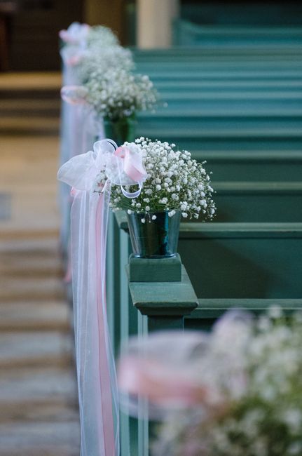 A decorative row of wedding flowers arranged in small, dark metal vases with vibrant pink and white roses, complemented by baby's breath, and tied with pastel pink and white ribbons, is displayed alon