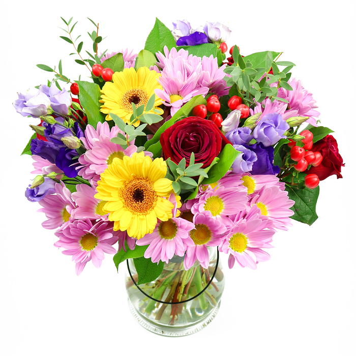 A beautifully balanced mixed-flower arrangement rises from a clear glass vase, the blooms gathered in a full, rounded shape and set against a crisp white background. At the centre of the bouquet, deep red roses unfold in layered, velvety petals, their rich hue giving the design a classic, romantic anchor. Close by, two golden yellow gerberas with dark brown-orange centres stand proudly, their wide, daisy-like faces injecting a sense of joy and brightness, like the sun catching the tops of trees around Cockfosters on a clear afternoon. Draped around these focal flowers is a generous garland of soft pink daisies or chrysanthemums. Each head is composed of many slim petals circling a tiny yellow centre, forming a plush, cushiony texture that gives the arrangement both volume and a gentle, comforting tone. Interwoven through these pastel blooms are slender stems of lisianthus in shades of purple and pale lavender, their bell-shaped petals adding a refined coolness and subtle movement. Tucked throughout the bouquet, glossy red hypericum berries form small, round clusters that bring playful, jewel-like highlights and an appealing textural contrast. A mixture of greenery wraps the composition: broad, deep green leaves give structure and weight, while lighter, more delicate foliage adds airiness and a freshly picked-from-the-garden feel. The transparent glass vase reveals the neatly trimmed stems, fanned out into clear water, emphasising the tidy craftsmanship of the florist and grounding the lush display above. The arrangement evokes a sense of celebration and thoughtful care, ideal for decorating a dining table in a Cockfosters home, greeting guests at a local gathering, or arriving as a surprise same-day delivery for a special occasion.
